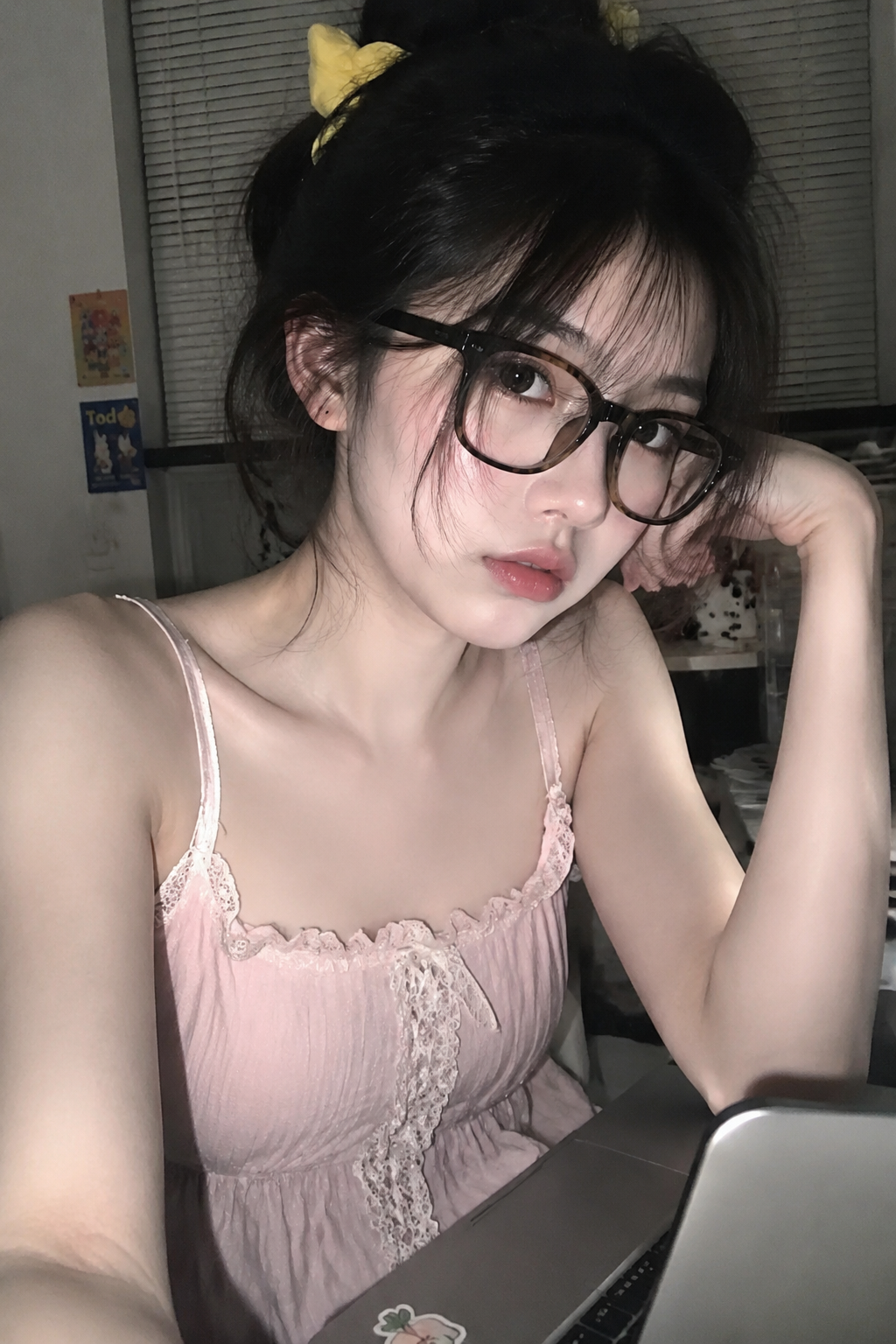 人像摄影，日常快照风格，非精心构图或打光，上半身特写，神情忧郁妖冶少女，冷白皮，时尚穿搭，瓜子脸尖下巴，皮肤白皙，底妆通透，肤色均匀自然，纯欲风 。发丝清晰可见，底部通透，肤色均匀自然，纯欲风。光线柔和自然，非均匀打光，表情自然松弛，照片毫无修饰感，带有生活真实感。ccd拍照感，iphone实拍，真人，真实生活， 人物形象：年轻女性、韩式甜美风、精致五官，身材匀称 发型：低蓬松盘发、黄色发圈、微乱碎发 服饰：粉色吊带裙、蕾丝花边设计、收腰版型 配饰：黑色粗框眼镜、复古文艺风 妆容：清透底妆、自然眼妆 场景动作：居家办公、使用笔记本电脑、日常自拍风格